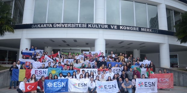 A large group of people with both national and ESN flags standing in front of the host University.